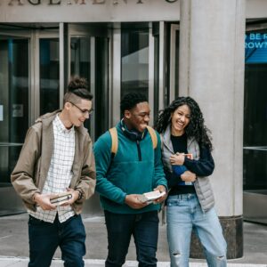 Young cheerful multiethnic students with books having fun on urban pavement while speaking in daylight